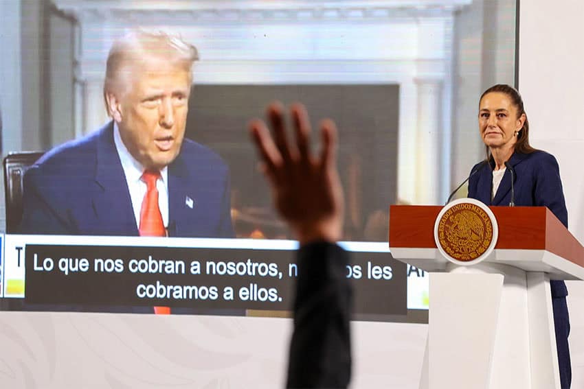 President Sheinbaum stands at a podium next to a projected video of Donald Trump, with the raised hand of a reporter visible in the foreground