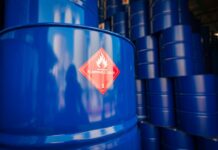 Blue barrels of oil stacked high in rows. One in front has a sticker saying "flammable liquid" on it.