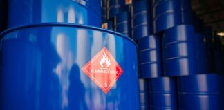 Blue barrels of oil stacked high in rows. One in front has a sticker saying "flammable liquid" on it.