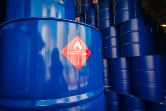 Blue barrels of oil stacked high in rows. One in front has a sticker saying 