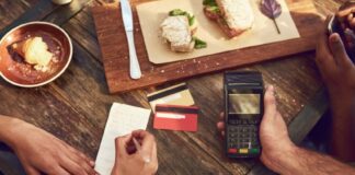 A server holds a payment terminal next to a restaurant table, while a diner signs their bill