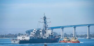 Tug boats pull the USS Spruance warship out to sea in San Diego