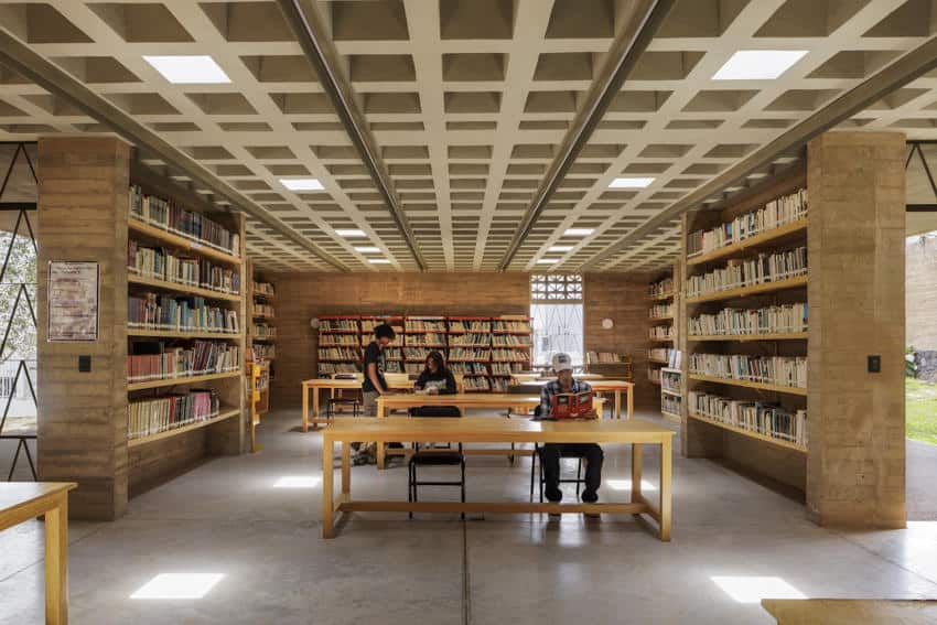 Geuthebac, Morlos, residents sit in a wide wood table in a library placed in a library filled with books.