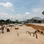 Man in shorts and no shirt in Jiutepec, Mexico, doing tricks on a skateboard in a skate park. There are no other people in the park.