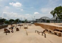 Man in shorts and no shirt in Jiutepec, Mexico, doing tricks on a skateboard in a skate park. There are no other people in the park.