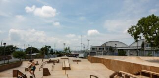 Man in shorts and no shirt in Jiutepec, Mexico, doing tricks on a skateboard in a skate park. There are no other people in the park.