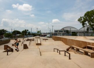 Man in shorts and no shirt in Jiutepec, Mexico, doing tricks on a skateboard in a skate park. There are no other people in the park.