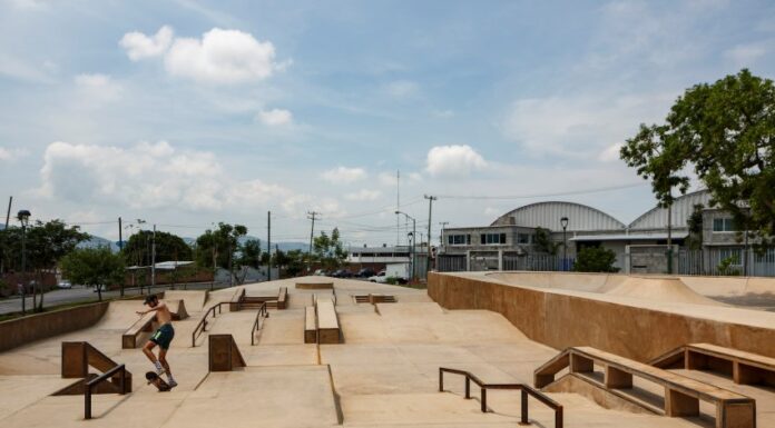Man in shorts and no shirt in Jiutepec, Mexico, doing tricks on a skateboard in a skate park. There are no other people in the park.