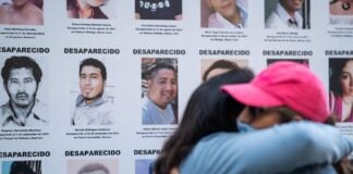 Two people hug in front of a poster showing names and photos of missing and disappeared people