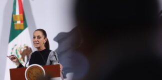 Claudia Sheinbaum stands at the presidential podium during her daily press conference, talking about US tariffs