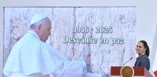 President Sheinbaum at a podium in front of screen honoring the life of Pope Francis