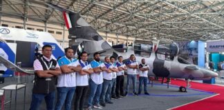 A team of engineers stands arms crossed in front of a small airplane