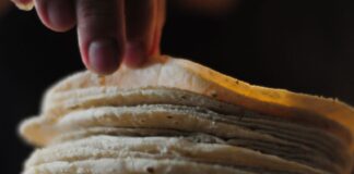 A stack of tortillas with a hand at the top, pulling a couple of tortillas off the stack.