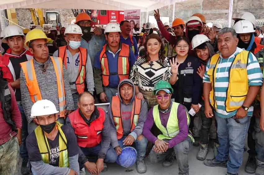 A group of construction workers in yellow and orange vests and hard hats posing for a group photo with two female politicians