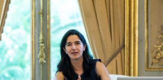 Mexican architect Fernanda Canales sitting at a luxurious wood table with small, glass water pitchers and a wine glass half filled with water.