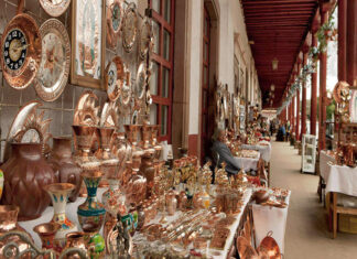 An artisan fair in a Mexican courtyard in a small town where hundreds of coppersmithed decorative objects are laid out on tables.