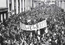 Black and white photo of crowds filling the streets of Mexico City in 1944 carrying a large banner saying "Viva el 1 de Mayo"