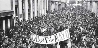 Black and white photo of crowds filling the streets of Mexico City in 1944 carrying a large banner saying "Viva el 1 de Mayo"