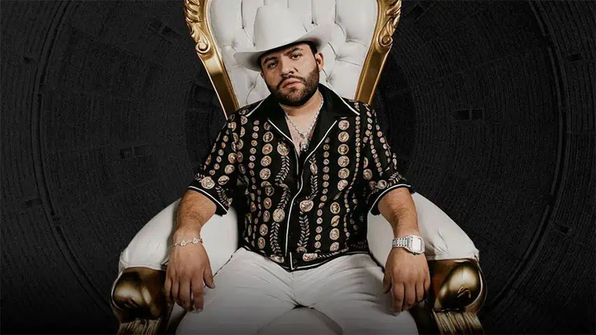 Luis R Conriquez sits in a throne-like gold and white chair wearing cowboy hat.