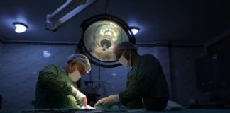 Two surgeons in scrubs and masks performing surgery in a dimly lit hospital operating room