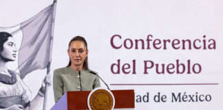 President Claudia Sheinbaum stands at a podium in front of a banner showing a Mexican flag and the words "Conferencia del Pueblo"