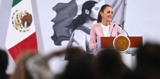 Sheinbaum stands smiling at a podium