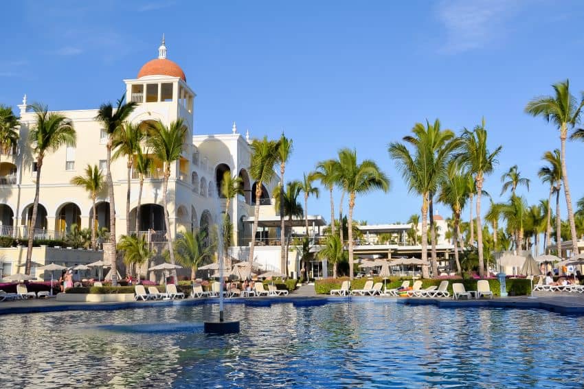 Outdoor swimming pool to Riu Hotel in Los Cabos, Mexico, with the white stone facade of the hotel in the background, done in a faux-Spanish hacienda architectural style.