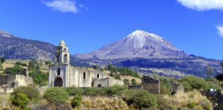 A snow and glacier-capped volcano with an old church in the foreground