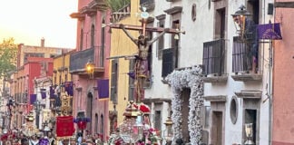 Men in black suits parade down a San Miguel de Allende street holding a figure of Christ on the cross over their heads.