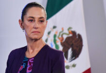 Claudia Sheinbaum with a serious expression and a Mexican flag