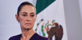Claudia Sheinbaum with a serious expression and a Mexican flag