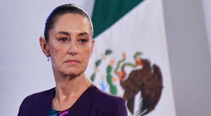 Claudia Sheinbaum with a serious expression and a Mexican flag