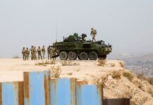 A US military tank and troops on a bluff behind the Mexico-US border wall