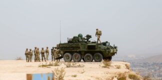 A US military tank and troops on a bluff behind the Mexico-US border wall