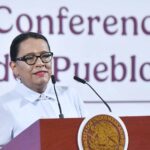A dark-haired woman speaks at a podium emblazoned with the emblem of the Mexican government.