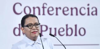 A dark-haired woman speaks at a podium emblazoned with the emblem of the Mexican government.