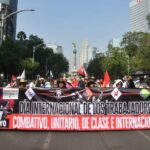 Protesters hold a large banner reading "International workers' day" in Spanish, in front of the Mexico City Angel of Independence monument
