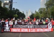 Protesters hold a large banner reading "International workers' day" in Spanish, in front of the Mexico City Angel of Independence monument