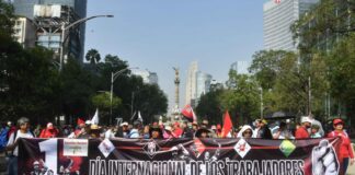 Protesters hold a large banner reading "International workers' day" in Spanish, in front of the Mexico City Angel of Independence monument