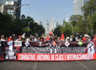 Protesters hold a large banner reading "International workers' day" in Spanish, in front of the Mexico City Angel of Independence monument