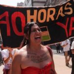 A woman at a protest shouts, standing in front of a sign reading "40 hours now" in Spanish