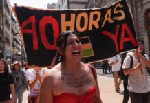 A woman at a protest shouts, standing in front of a sign reading "40 hours now" in Spanish
