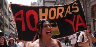 A woman at a protest shouts, standing in front of a sign reading "40 hours now" in Spanish