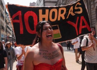 A woman at a protest shouts, standing in front of a sign reading "40 hours now" in Spanish