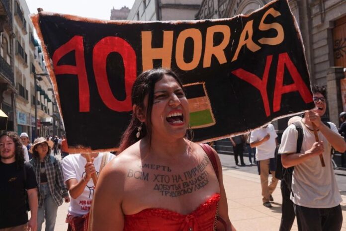 A woman at a protest shouts, standing in front of a sign reading 