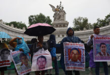 Protesters hold signs showing the faces of the disappeared on a rainy day in front of a Mexico City landmark