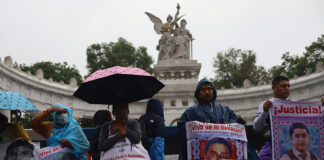 Protesters hold signs showing the faces of the disappeared on a rainy day in front of a Mexico City landmark