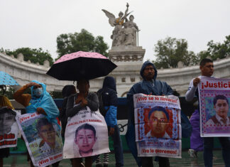 Protesters hold signs showing the faces of the disappeared on a rainy day in front of a Mexico City landmark