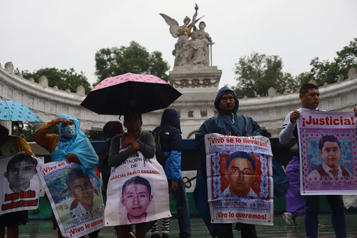 Protesters hold signs showing the faces of the disappeared on a rainy day in front of a Mexico City landmark