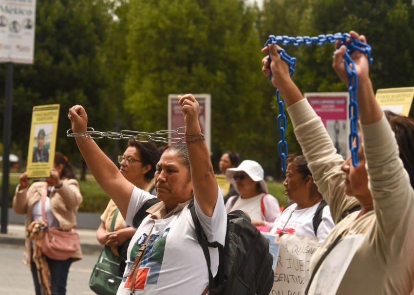 A group of Mexican women in Toluca, Mexico state, standing in rows on the street holding thick chains above their heads.